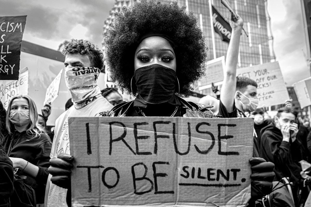 Picture of a woman of colour standing with a banner reading I refuse to be silent